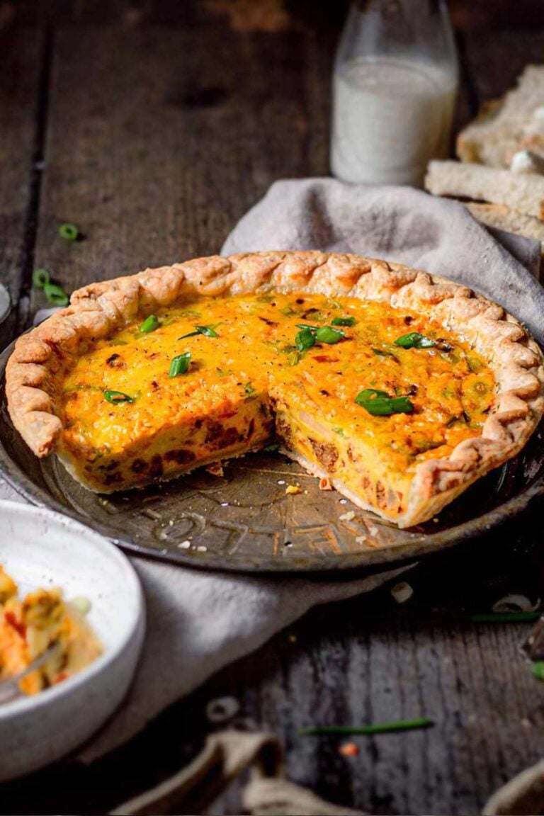 Whole vegan Just Egg quiche in a pie dish with a slice removed, showing creamy eggy filling and topped with green onions.
