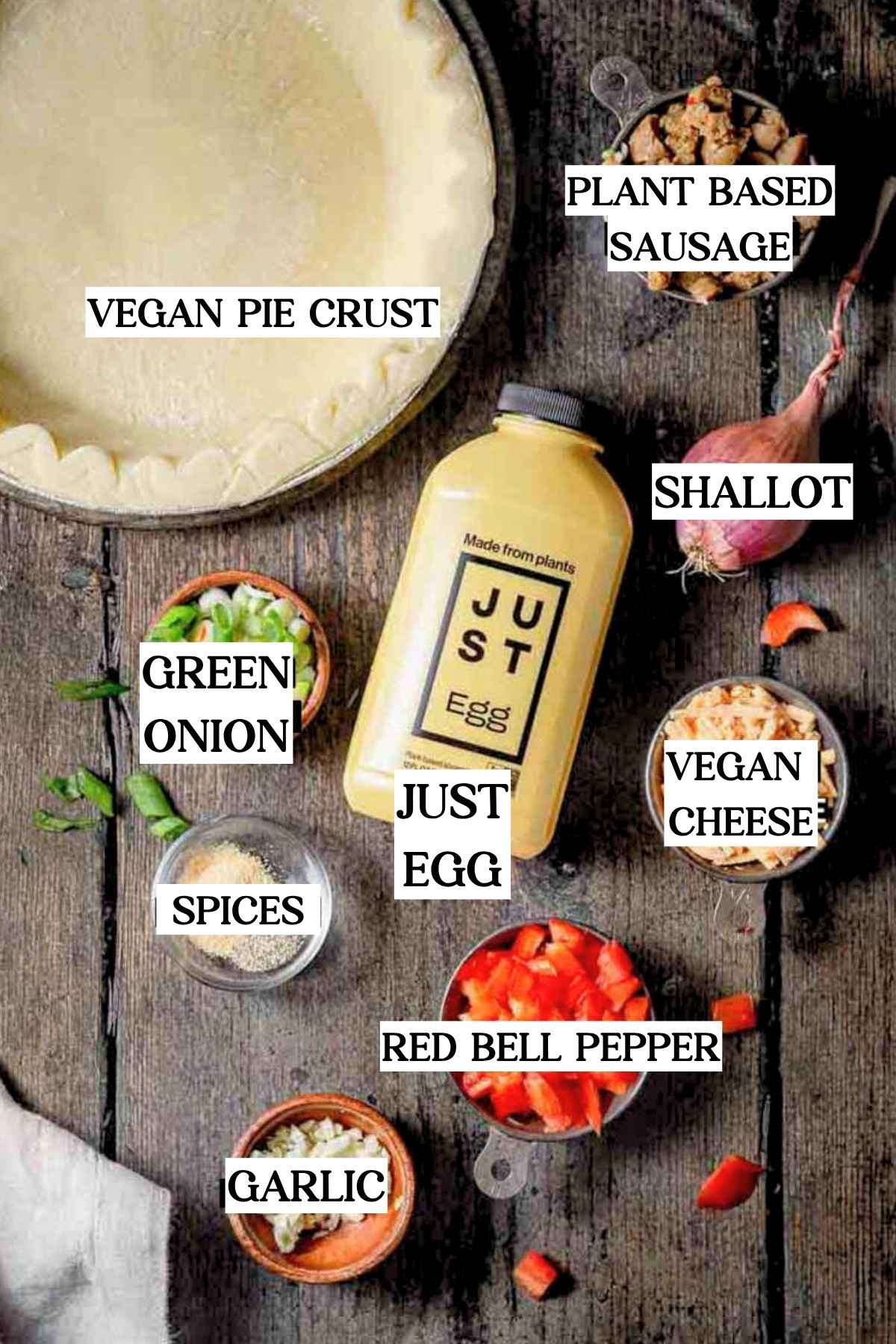 Labeled overhead image of ingredients for vegan Just Egg quiche including vegan pie crust, Just Egg bottle, plant-based sausage, bell pepper, green onion, shallot, garlic, spices, and vegan cheese.
