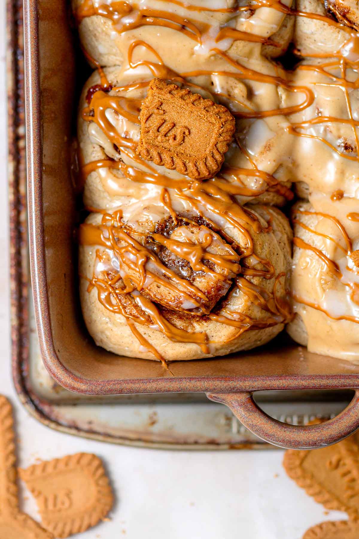 a top view of a gooey biscoff cookie butter cinnamon roll in a brown ceramic baking dish.
