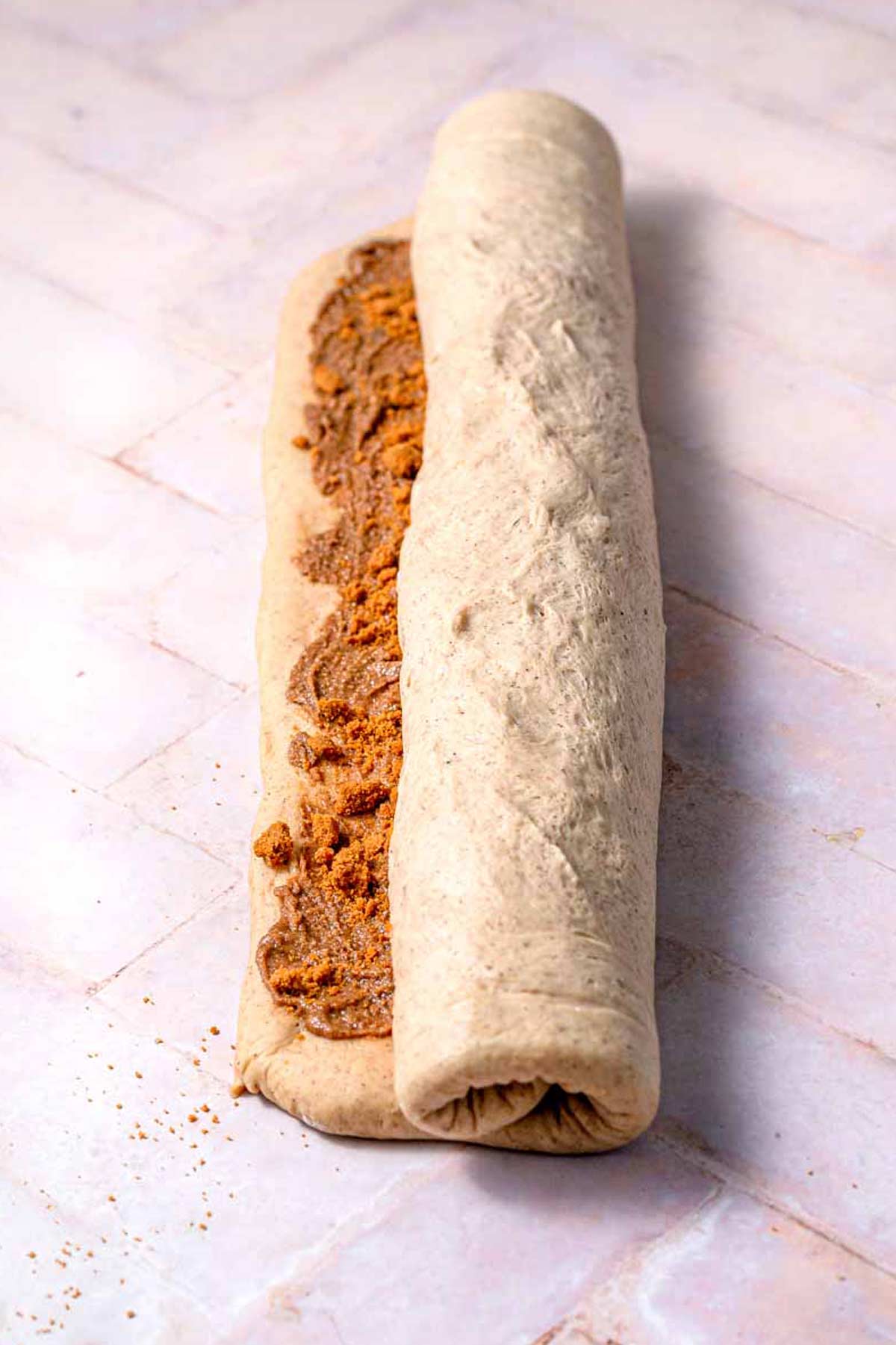 the Biscoff cinnamon roll dough being rolled into a long log.
