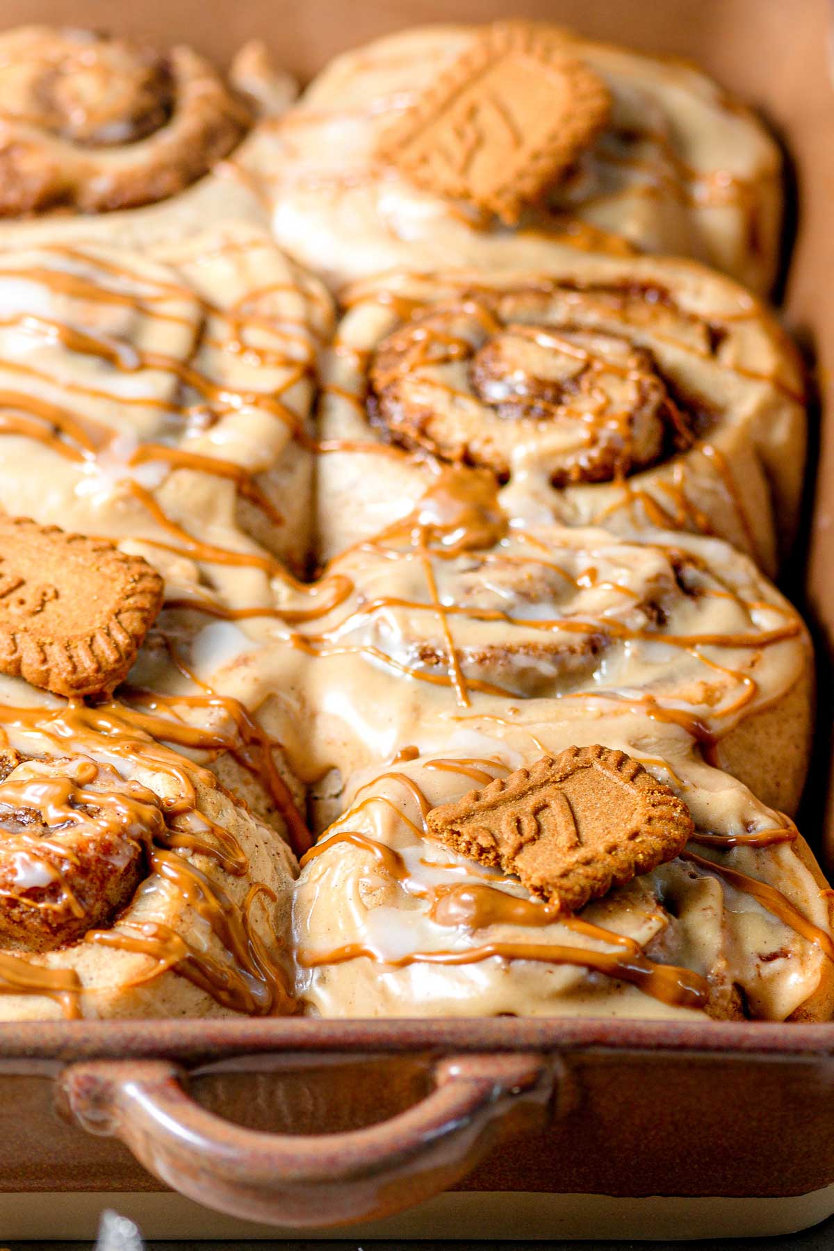 baked biscoff cinnamon rolls in a baking dish with cookie butter cream cheese frosting.