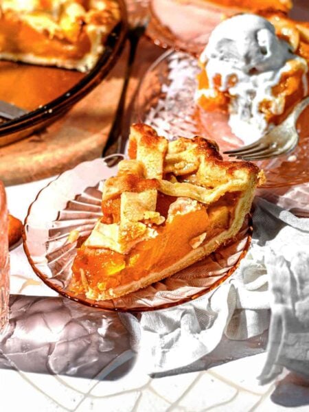 a sliced of peach pie made from canned peaches with a lattice crust on a glass pie plate.