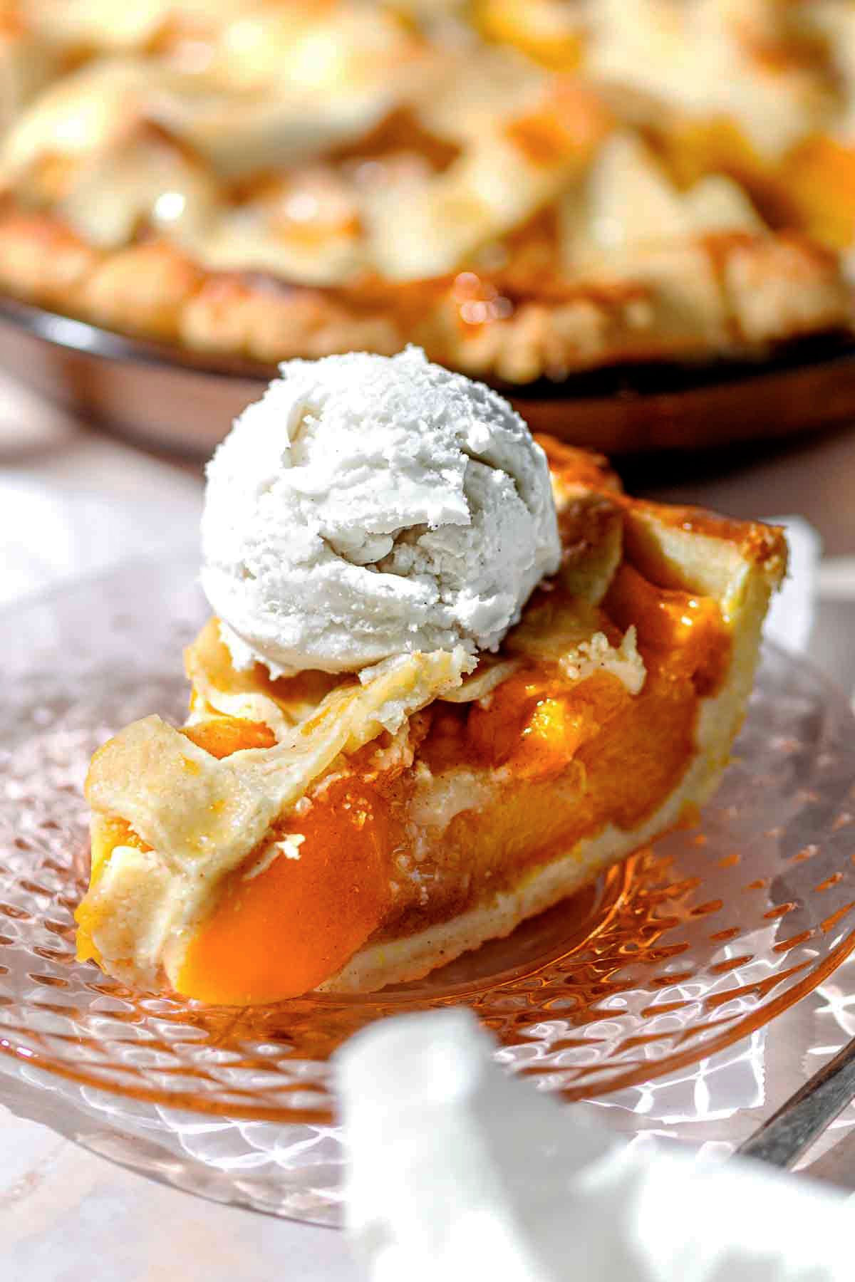a slice of peach pie with canned peaches on a pink plate with a scoop of ice cream.
