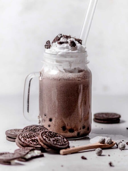 oreo bubble milk tea in a glass with whipped cream and a glass straw.