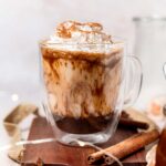 vegan iced pumpkin spice latte with oat milk in a glass on a cutting board.