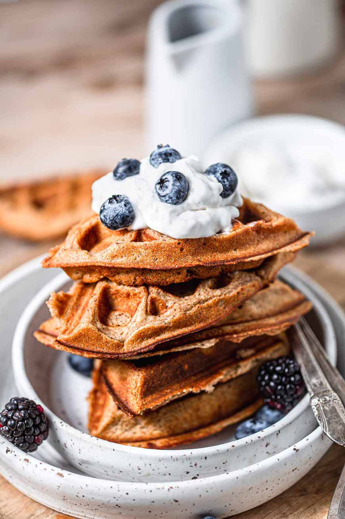 a stack of vegan protein waffles with dairy-free whipped cream and blueberries.