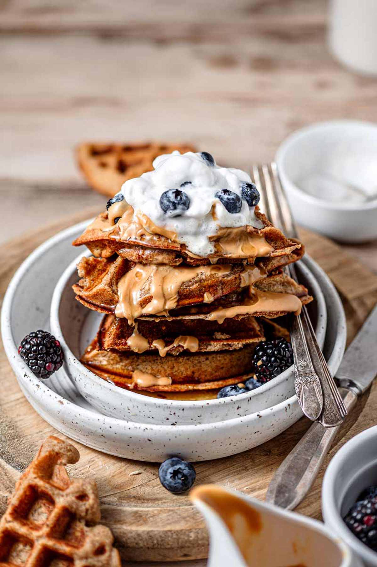a stack of vegan protein waffles with nut butter, berries and dairy-free whipped cream.