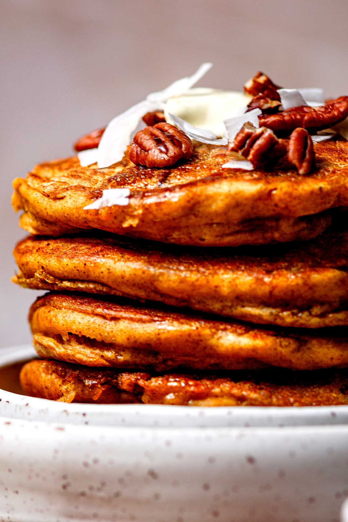 a stack of fluffy vegan pumpkin pancakes with pecans and coconut flakes.