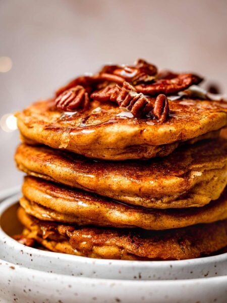 a stack of fluffy vegan pumpkin spice pancakes with pecans on top.