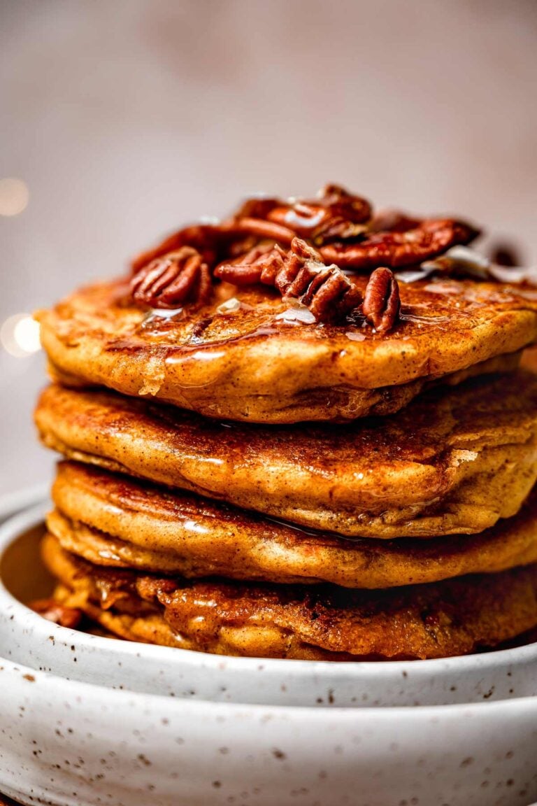 a stack of fluffy vegan pumpkin spice pancakes with pecans on top.