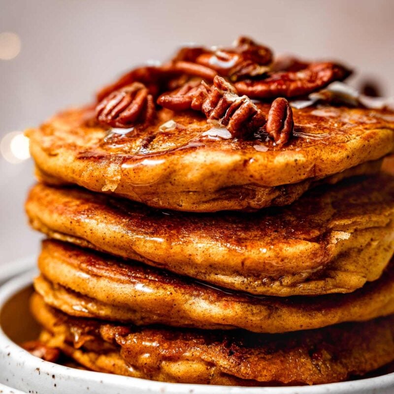 a stack of fluffy vegan pumpkin spice pancakes with pecans on top.