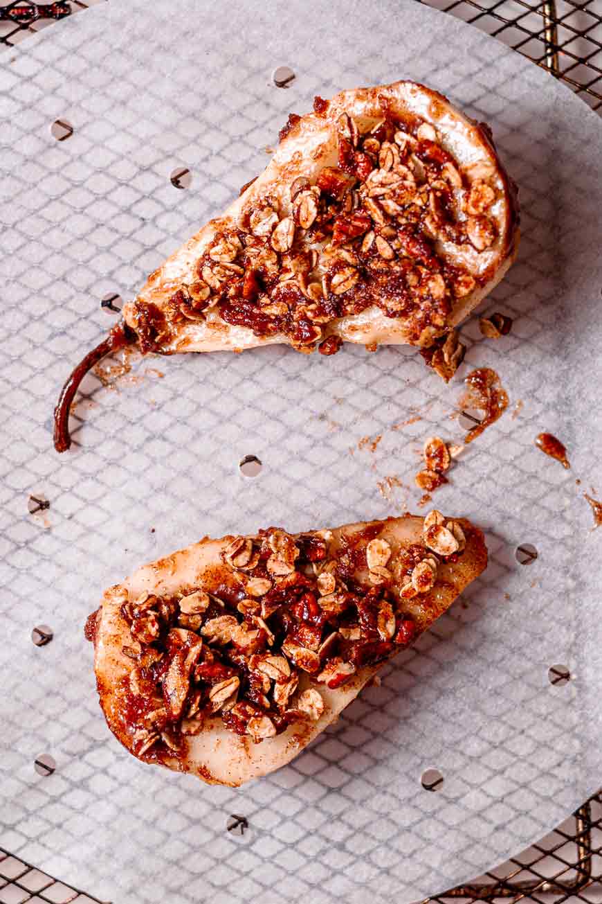 two pear halves with oat crumble on a parchment lined air fryer basket.