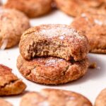 two vegan snickerdoodle cookies stacked on each other on a baking sheet.