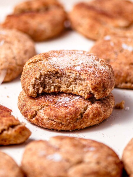 two vegan snickerdoodle cookies stacked on each other on a baking sheet.