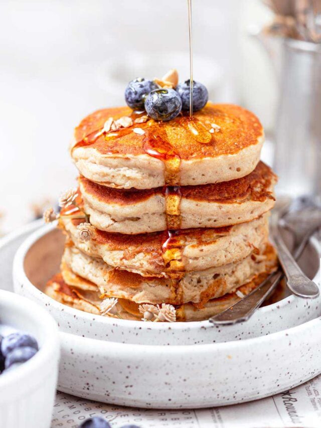Five Fluffy Oat milk Pancakes stacked on top of each other with maple syrup drizzling down on it