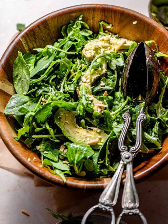 spinach arugula salad with lemon dressing in a wooden salad bowl.