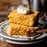 two pieces of eggless cornbread on a stack of white plates with a slice of vegan butter on top.