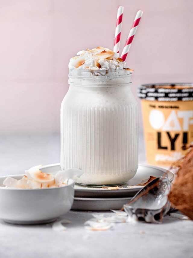 a coconut milkshake in a clear glass topped with toasted coconut and red straws.