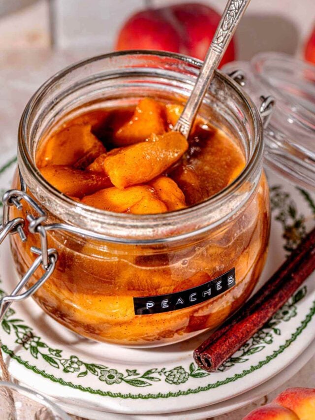stovetop stewed peaches with a vintage silver ladle in a glass storage container.
