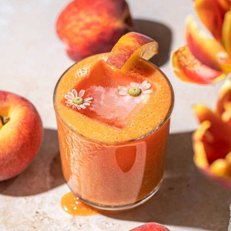 fresh peach juice in a small glass with an ice cube with flowers inside it.