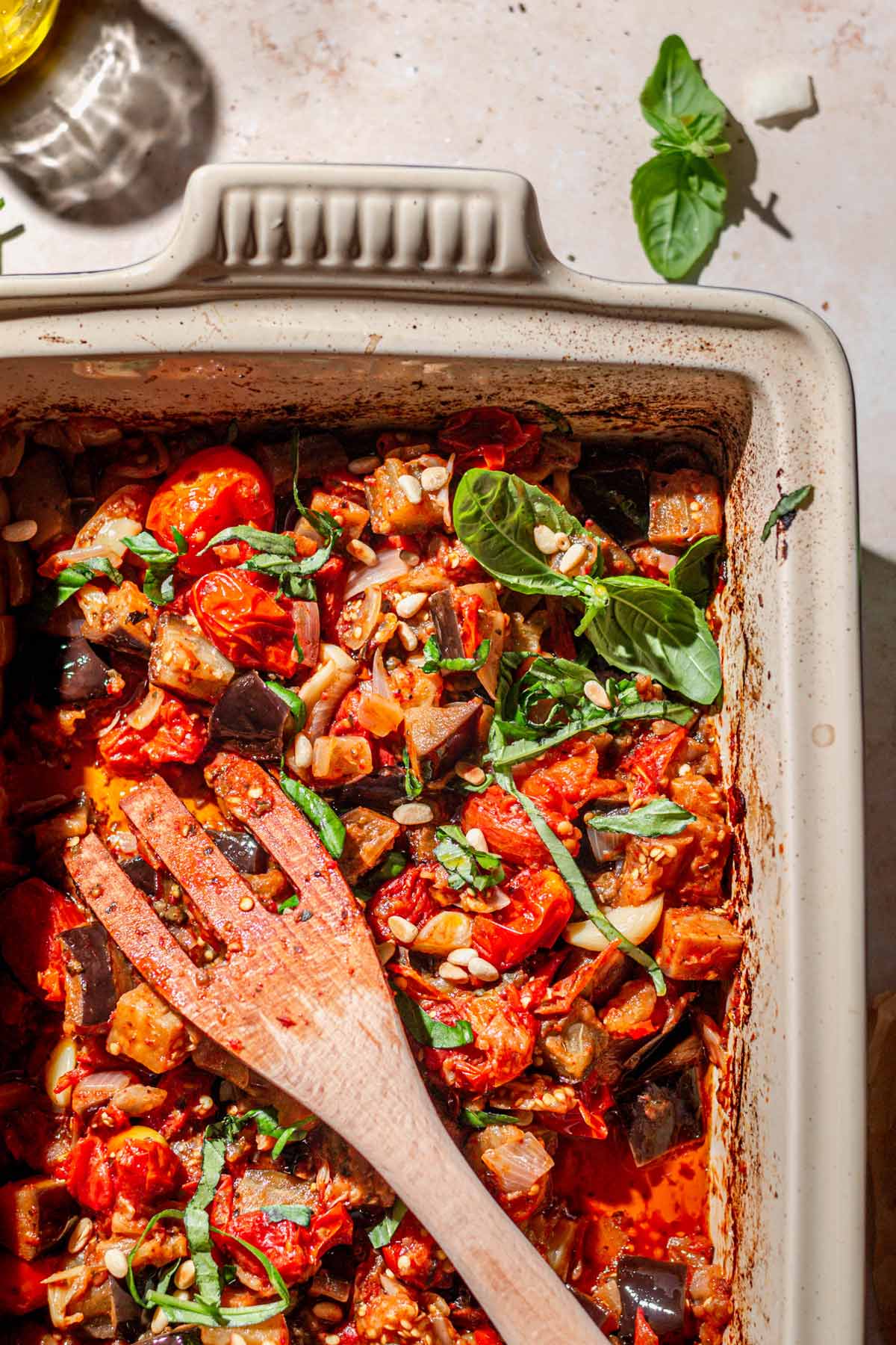 roasted eggplant and burst cherry tomatoes in a baking dish with a wooden spatula.