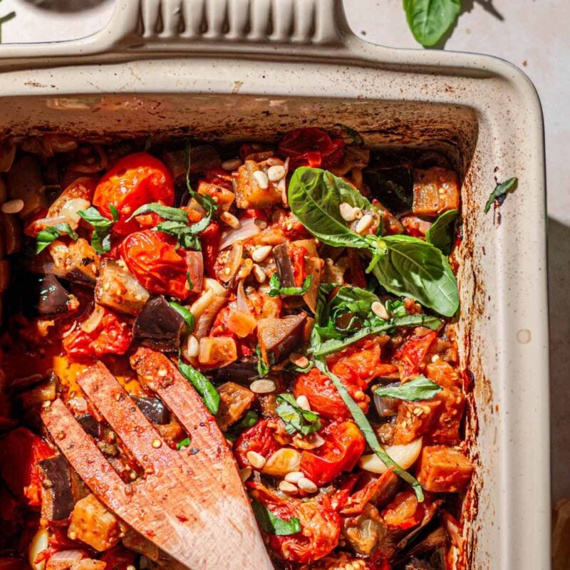 the roasted eggplant with tomatoes and basil in a baking dish with a wooden spatula.