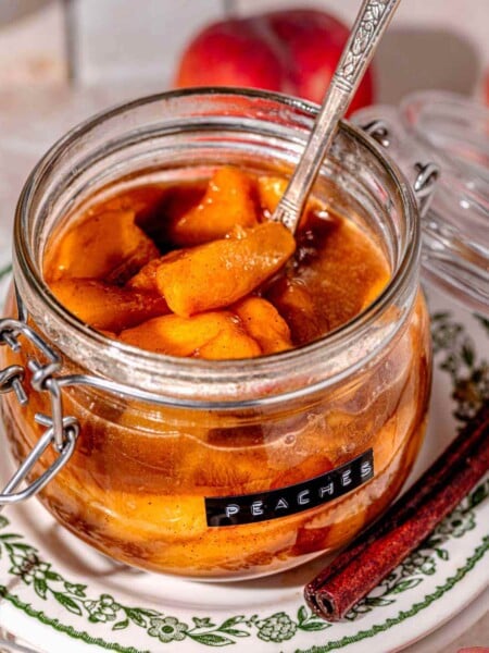 stovetop stewed peaches with a vintage silver ladle in a glass storage container.