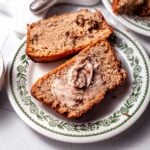two slices of vegan Bisquick Zucchini Bread on a vintage dessert plate with a smear of butter on top.