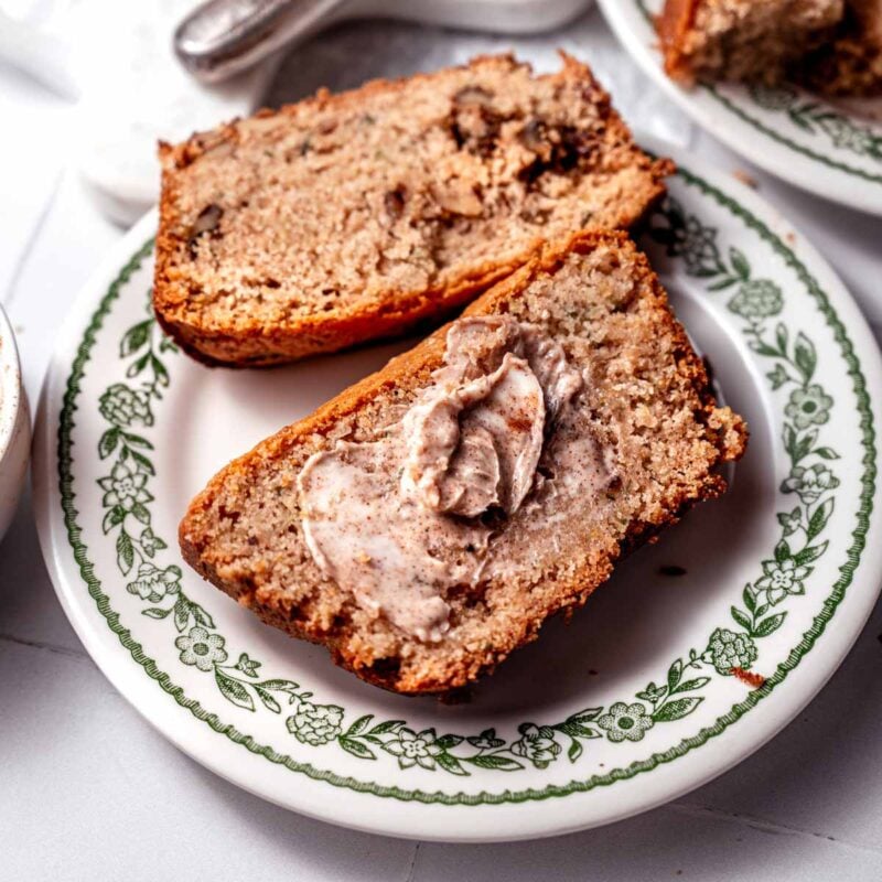 two slices of vegan Bisquick Zucchini Bread on a vintage dessert plate with a smear of butter on top.