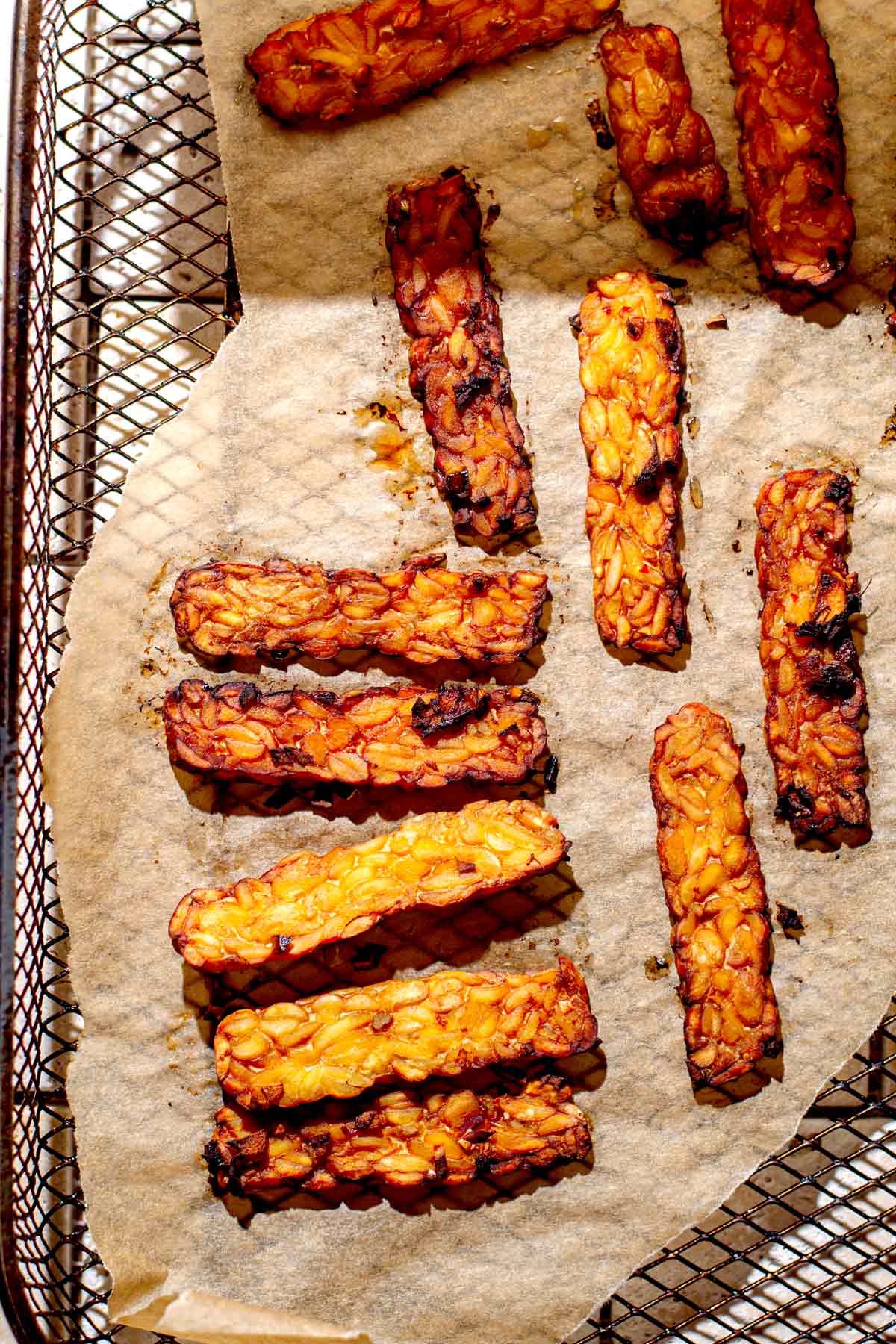 slices of fried tempeh in an air fryer basket lined with parchment paper.