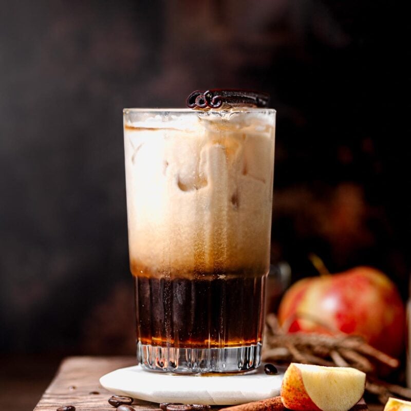 an apple crisp oatmilk shaken espresso in a tall glass on a coaster.