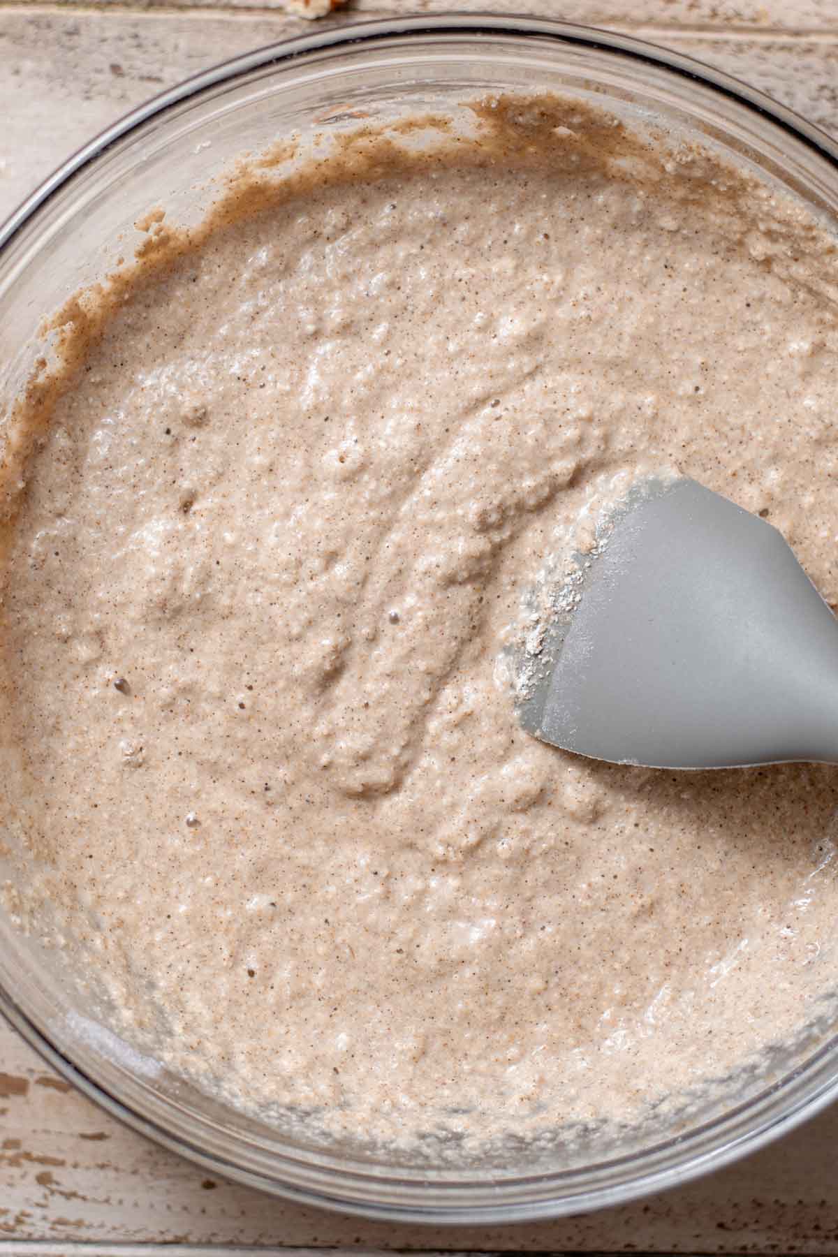 the apple oat cake batter in a glass bowl with a grey spatula.