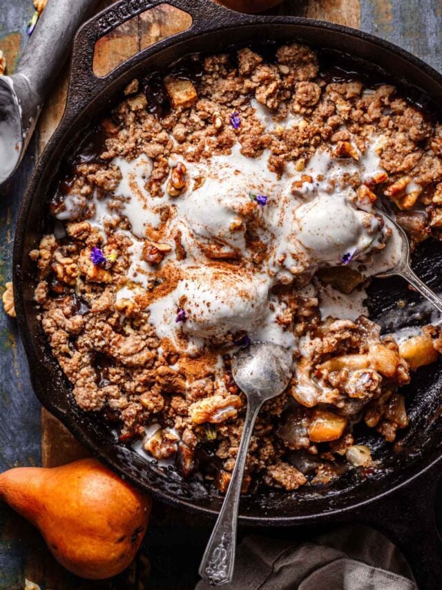 pear crumble with walnuts in a cast iron pan with ice cream on top.