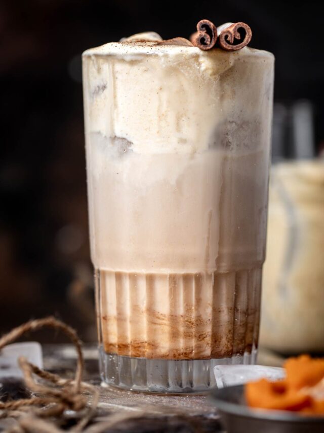 a starbucks copycat pumpkin cream chai latte in a tall glass with a cinnamon stick on top.