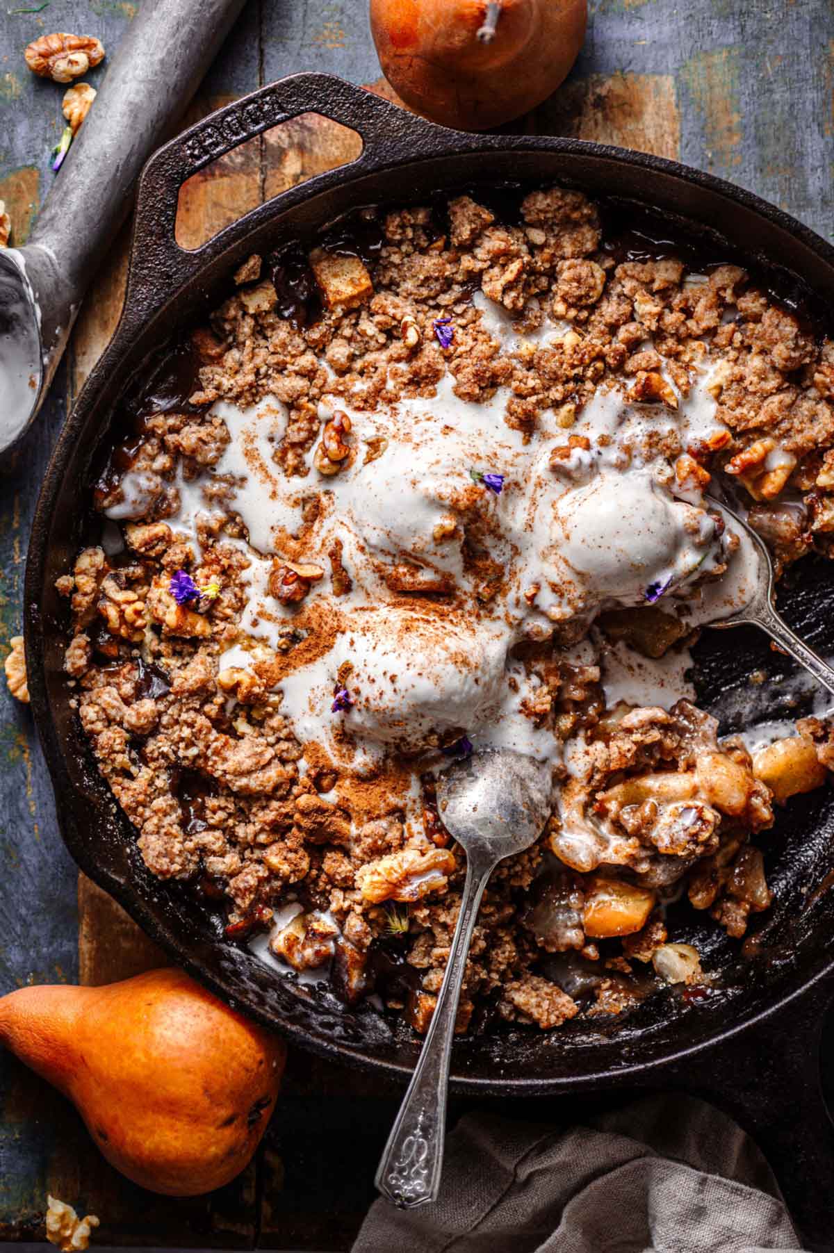 pear crumble with walnuts in a cast iron pan with ice cream on top.