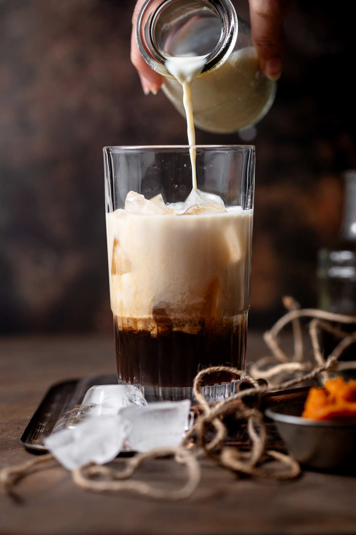 a hand pouring oat milk onto chai tea concentrate in a tall glass.