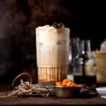 a starbucks copycat pumpkin cream chai latte in a tall glass with a cinnamon stick on top.