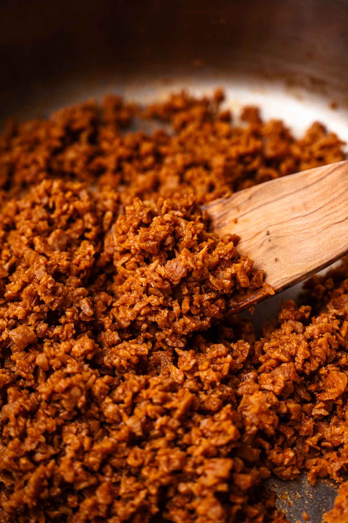 Vegan and vegetarian tvp ground beef in a stainless steel pan with a wooden spatula scooping some.