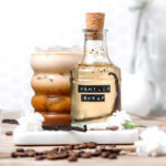homemade vanilla syrup in a glass jar with a cup of iced coffee.