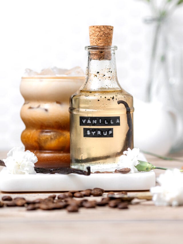 a bottle of vanilla syrup in front of a vanilla iced coffee.