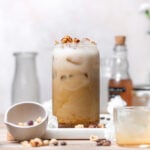 hazelnut latte in a tall glass with hazelnuts on top.