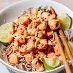 crispy baked bang bang tofu coated in sauce on a bowl of soba noodles.