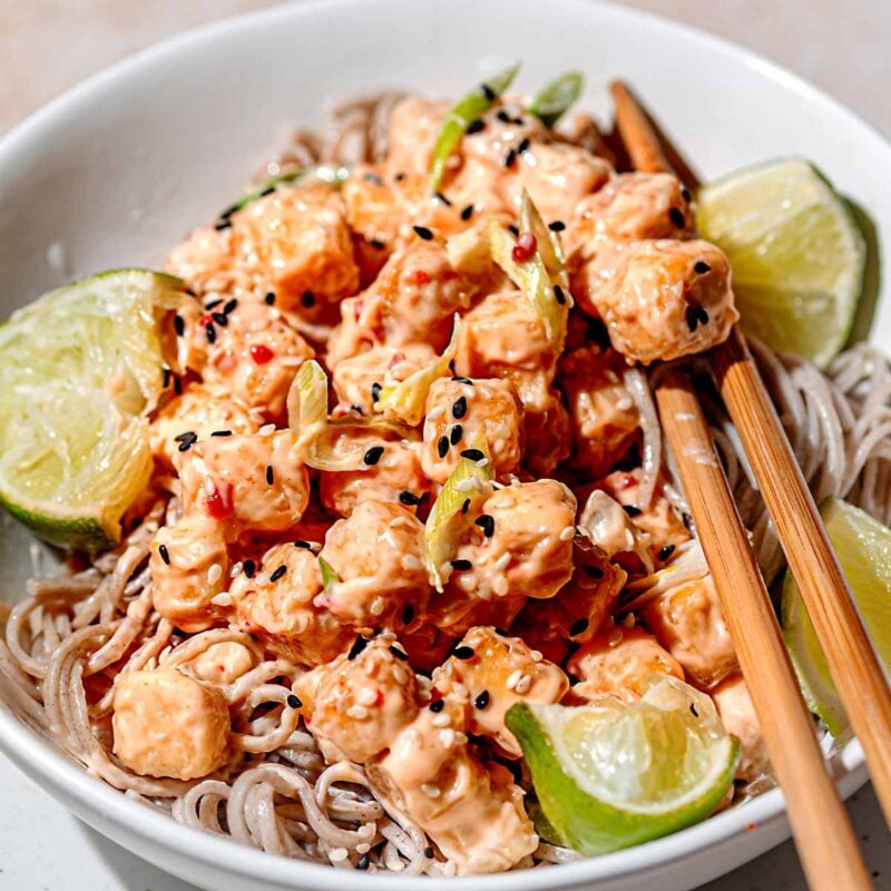 crispy baked bang bang tofu coated in sauce on a bowl of soba noodles.
