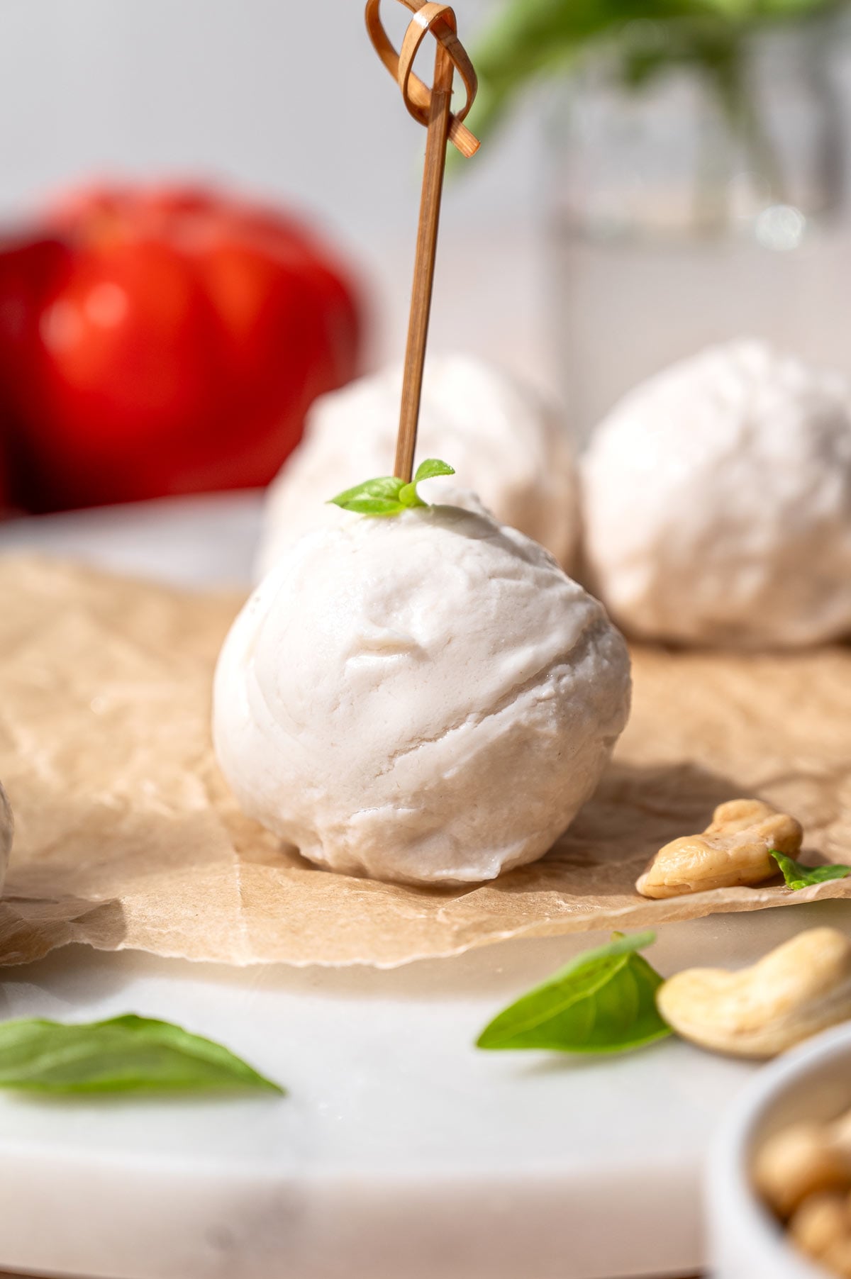 Homemade dairy-free mozzarella ball on parchment with fresh basil, cashews, tomatoes, and additional mozzarella in the background.