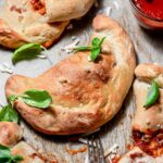vegan calzones with fresh basil on a baking sheet.