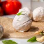 Close-up of a fresh vegan mozzarella ball topped with basil and arranged with cashews, tomatoes, and parchment paper.