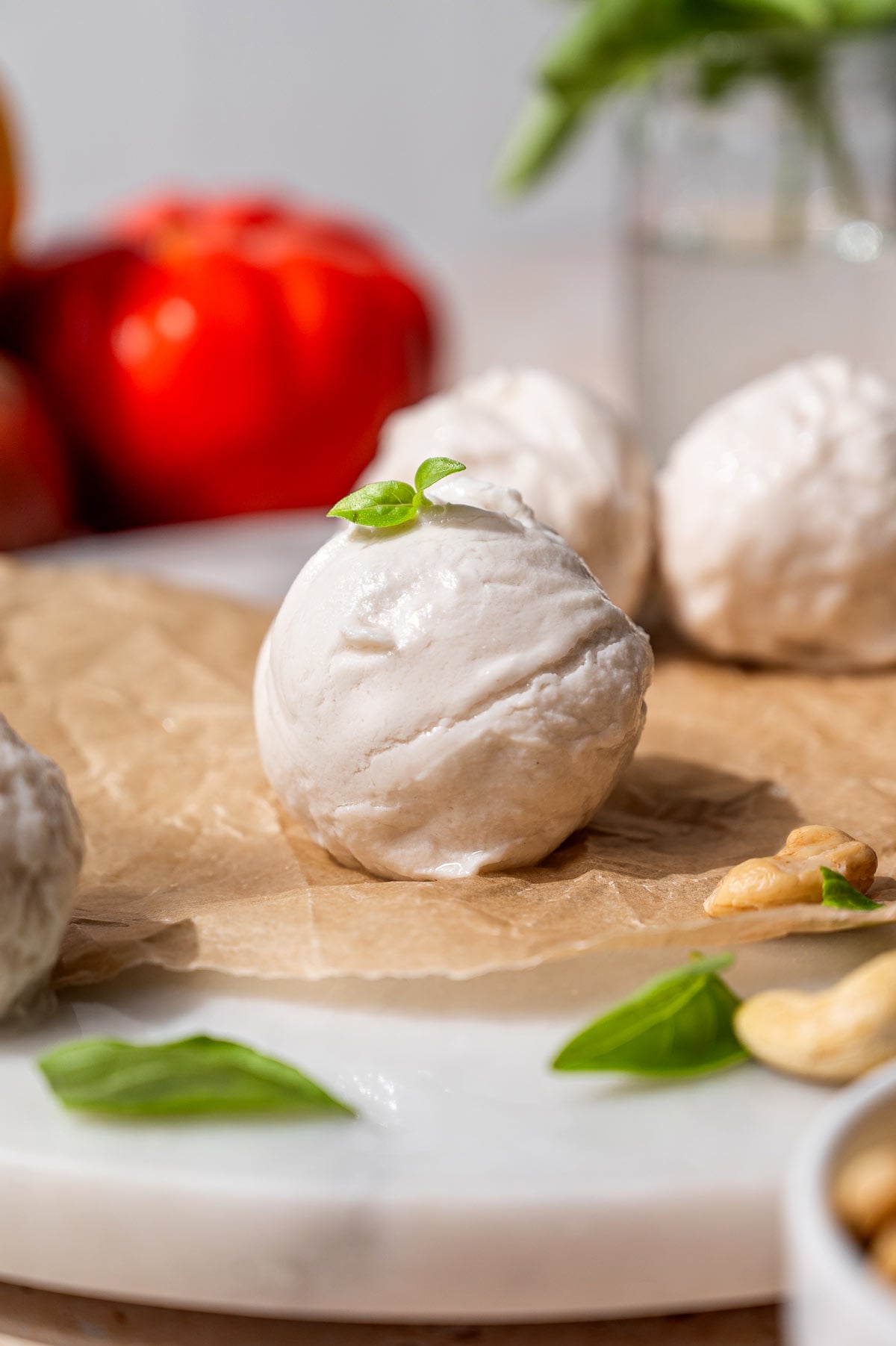 Close-up of a fresh vegan mozzarella ball topped with basil and arranged with cashews, tomatoes, and parchment paper.