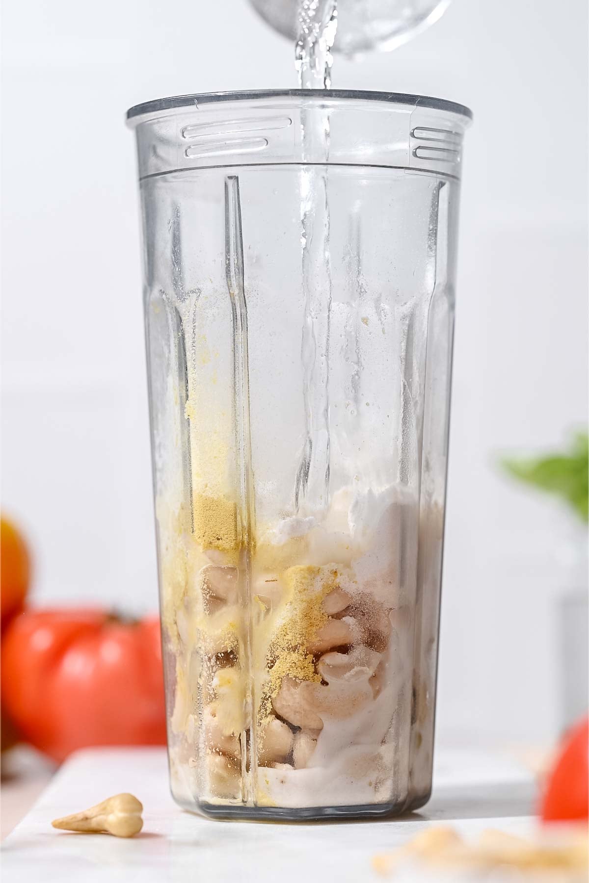 Water being poured into a blender cup filled with cashews, seasonings, and other mozzarella ingredients.