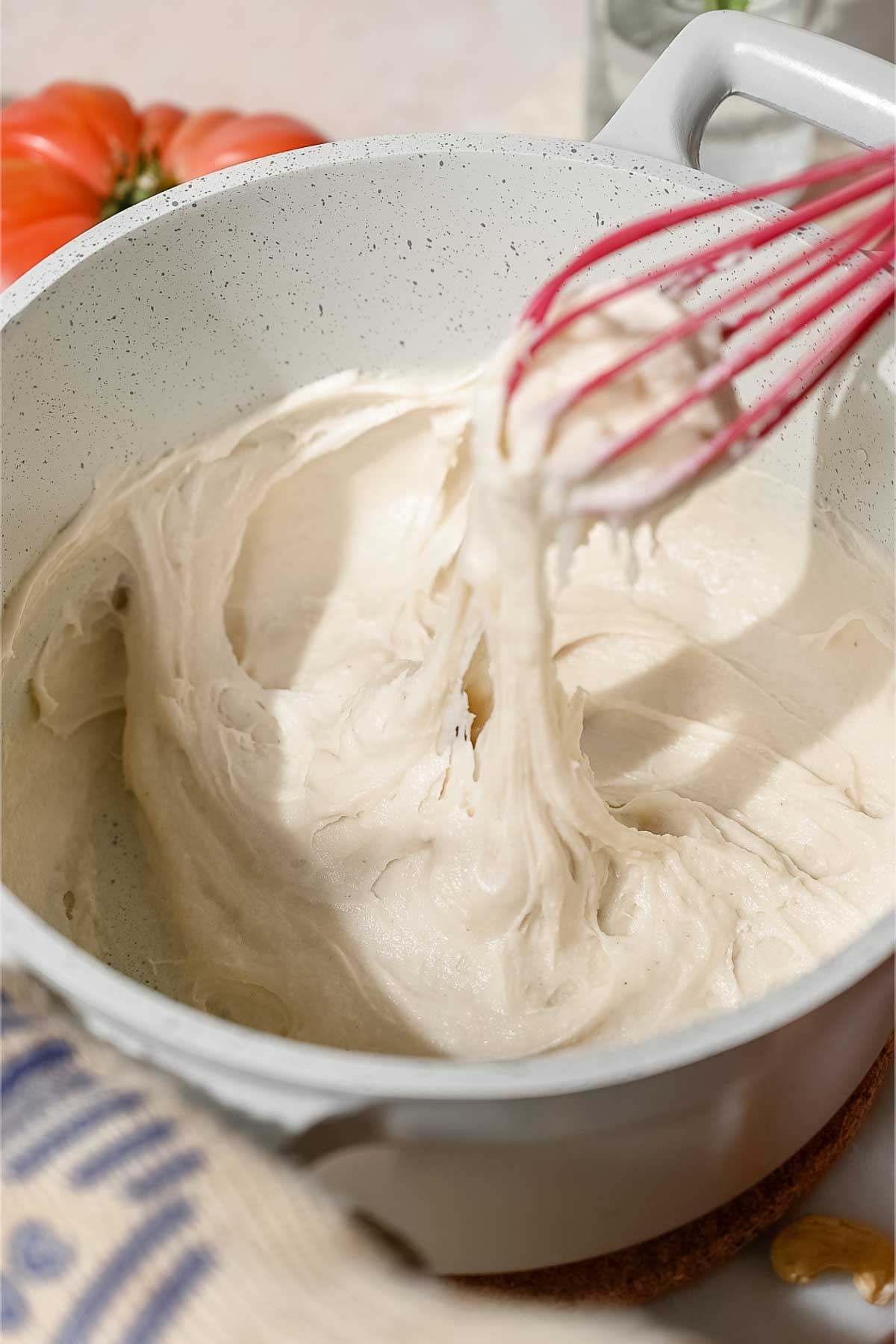 Thick, stretchy dairy-free mozzarella mixture clinging to a whisk as it cooks in a saucepan.