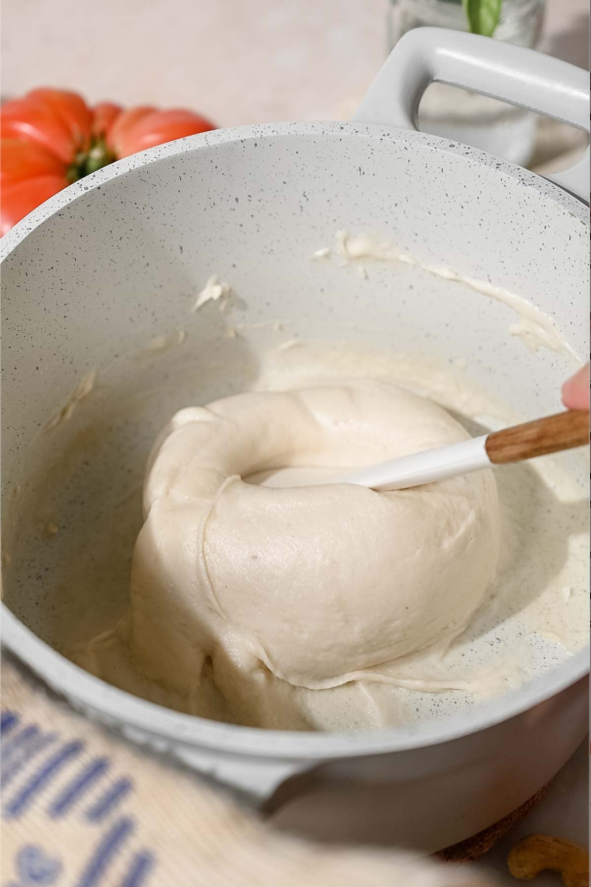 Thickened cashew mozzarella mixture being folded with a spatula until smooth and elastic.